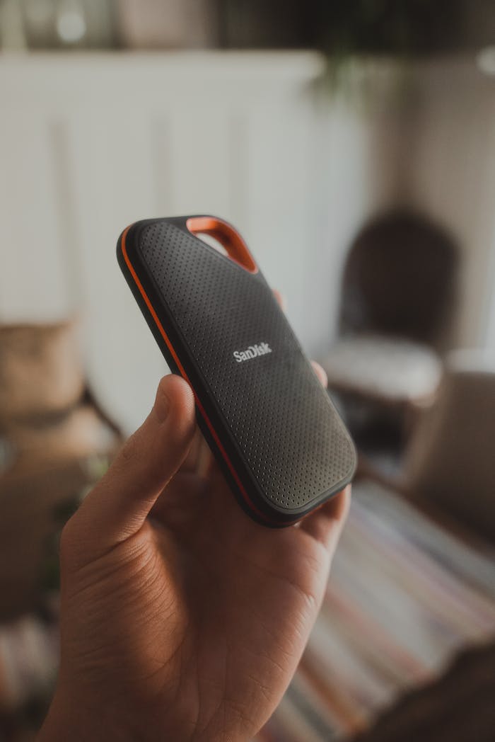 A SanDisk portable SSD being held in hand indoors with a blurred background.