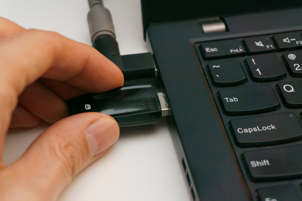 A close-up of a hand inserting a USB drive into a laptop port, highlighting technology and connectivity.